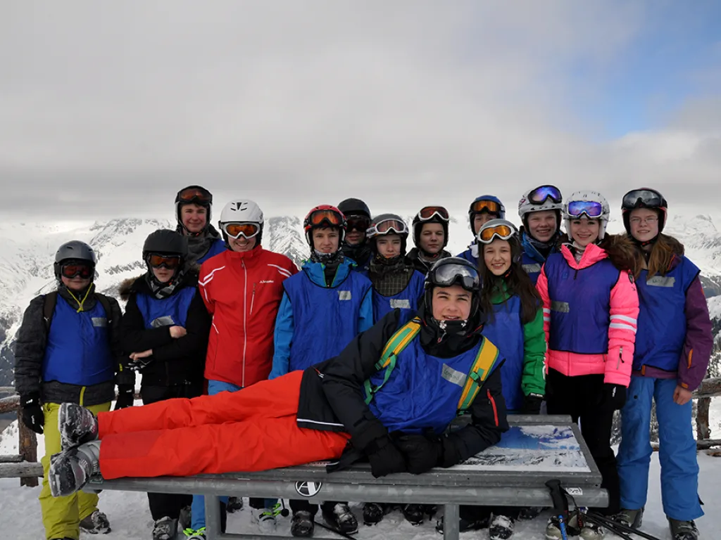 Gruppenfoto auf einer Holzbank vor Bergpanorama.